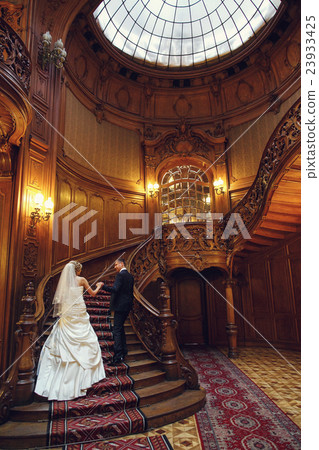 Groom and bride go upstairs in an old wooden hall 23933425