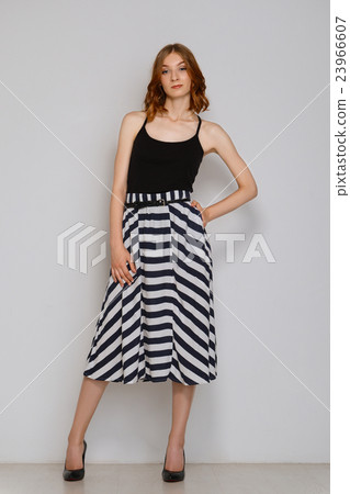 Pretty girl in skirt posing near white wall. Female legs in black shoes. Stript Pretty girl in skirt posing near white wall. Female legs in black shoes. Stript 23966607