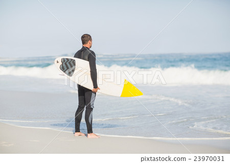 Rear view of man with surfboard standing on the beach Rear view of man with surfboard standing on the beach 23970031