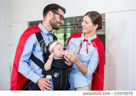Cheerful couple in superhero costume feeding milk to daughter Cheerful couple in superhero costume feeding milk to daughter 23970079