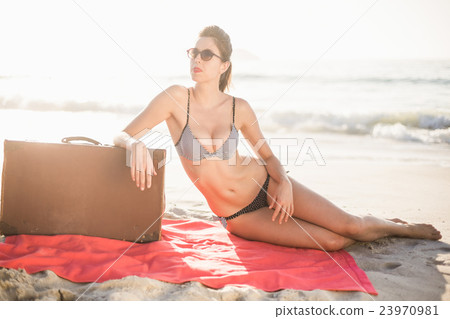 Glamorous woman in bikini sitting next to suitcase on the beach Glamorous woman in bikini sitting next to suitcase on the beach 23970981
