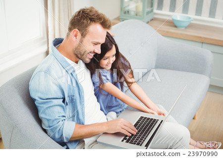 Smiling father and daughter using laptop while sitting on sofa Smiling father and daughter using laptop while sitting on sofa 23970990