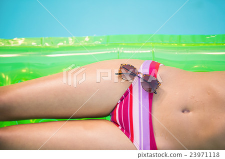 Mid section of a woman in bikini lying on air bed with sunglasse Mid section of a woman in bikini lying on air bed with sunglasse 23971118