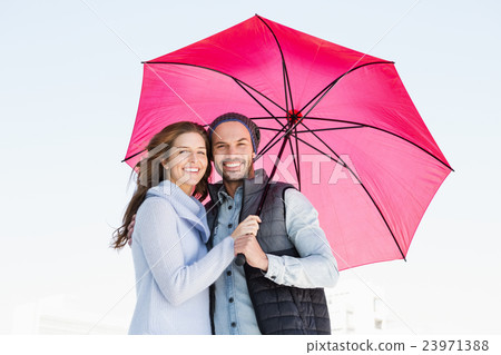 Happy young couple holding pink umbrella 23971388
