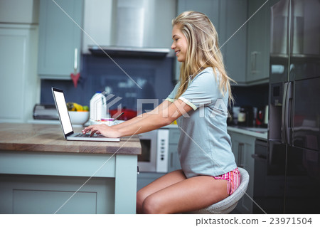 Happy beautiful woman using laptop at table in kitchen Happy beautiful woman using laptop at table in kitchen 23971504