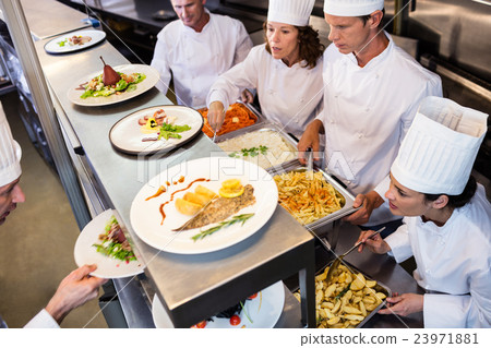 Chefs handing dinner plates through order station Chefs handing dinner plates through order station 23971881