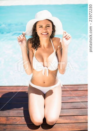 Happy woman in hat sitting by pool side 23972280