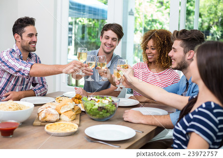 Young friends toasting wine while having meal at table Young friends toasting wine while having meal at table 23972757