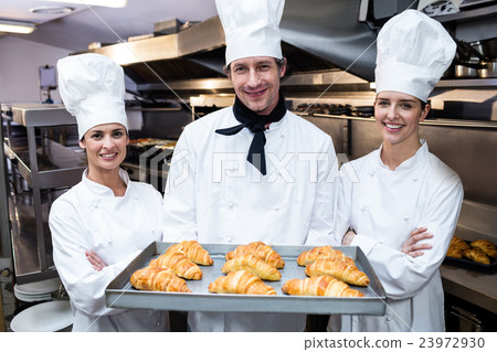 Three chefs holding a tray of baked croissant Three chefs holding a tray of baked croissant 23972930