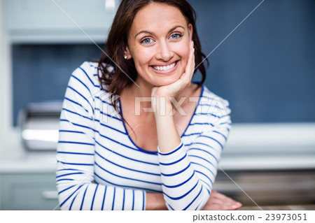 Portrait of happy young woman sitting at table in kitchen 23973051