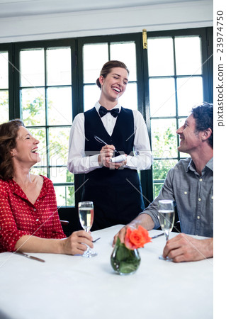 Young waitress laughing while taking an order from a couple Young waitress laughing while taking an order from a couple 23974750