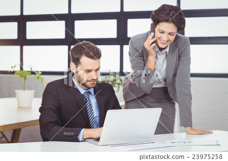 Business people with mobile phone and laptop in office Business people with mobile phone and laptop in office 23975258