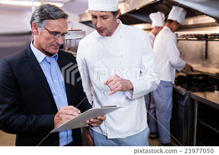 Male restaurant manager writing on clipboard while interacting t Male restaurant manager writing on clipboard while interacting t 23977050