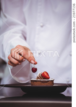 Chef putting a cherry on a dessert 23977136