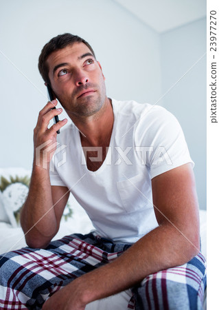 Man sitting on bed talking on phone 23977270