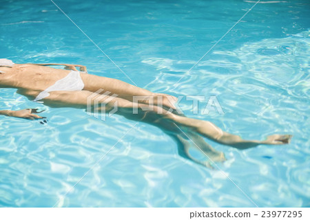 Woman in white bikini floating in swimming pool Woman in white bikini floating in swimming pool 23977295