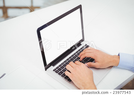 Businessman working on laptop at desk in office Businessman working on laptop at desk in office 23977543