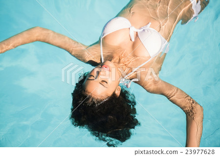 Beautiful woman in white bikini floating in swimming pool Beautiful woman in white bikini floating in swimming pool 23977628