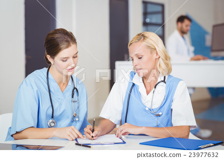Female doctor writing on paper while discussing with colleague 23977632
