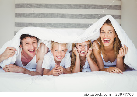 Portrait of family covered with duvet on bed 23977706