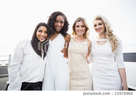 Well dressed women posing next to a limousine 23978968