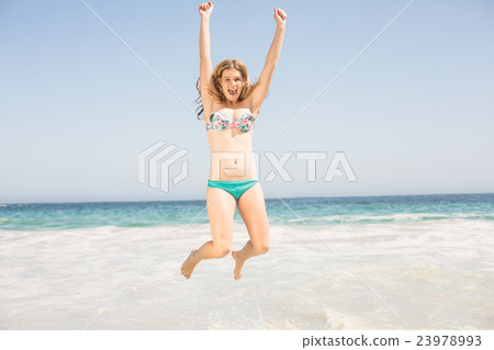 Carefree woman in bikini jumping on the beach Carefree woman in bikini jumping on the beach 23978993