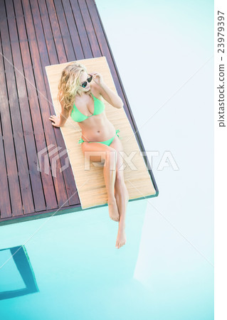Beautiful woman in green bikini relaxing by pool side Beautiful woman in green bikini relaxing by pool side 23979397