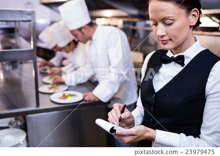 Waitress with note pad in commercial kitchen Waitress with note pad in commercial kitchen 23979475