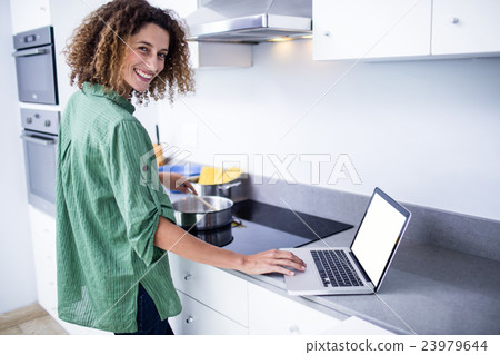 Portrait of woman working on laptop while cooking Portrait of woman working on laptop while cooking 23979644