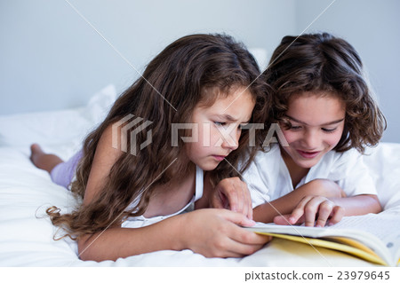 Brother and sister reading book together on bed Brother and sister reading book together on bed 23979645