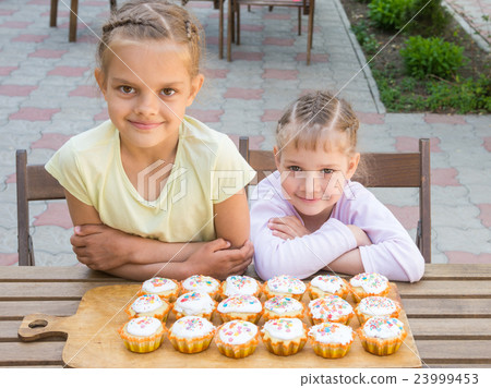 Two sisters sitting at a table on which are freshly baked Easter cupcakes 23999453