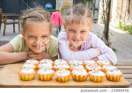 Two girls pretending funny faces, sitting in front of easter cupcakes 23999456