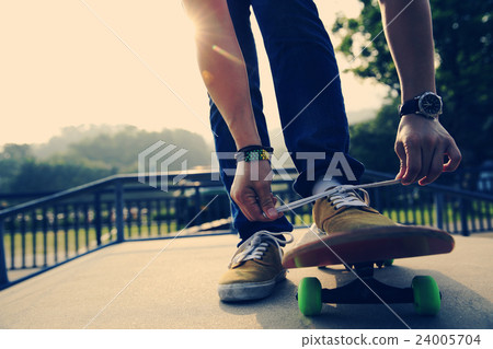 skateboarder tying shoelace at skatepark ramp 24005704