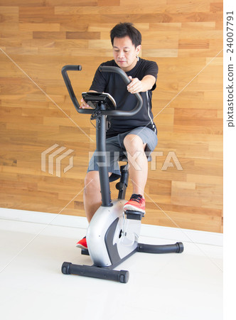 Asian Man On Excercise Bike At Fitness Center Asian Man On Excercise Bike At Fitness Center 24007791
