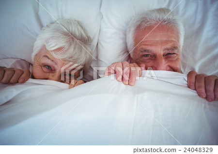 Portrait of happy senior couple hiding under blanket 24048329