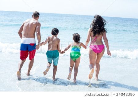 Rear view of family running towards sea Rear view of family running towards sea 24048390