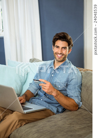 Portrait of young man sitting on sofa and shopping online on laptop Portrait of young man sitting on sofa and shopping online on laptop 24048539