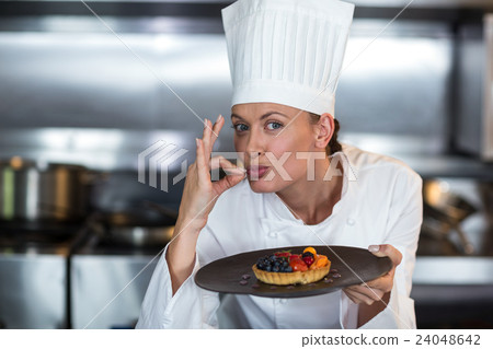 Portrait of female chef showing ok sign while holding dessert Portrait of female chef showing ok sign while holding dessert 24048642