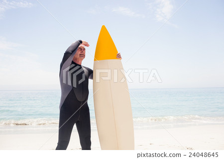 Senior man with surfboard shielding eyes at beach Senior man with surfboard shielding eyes at beach 24048645