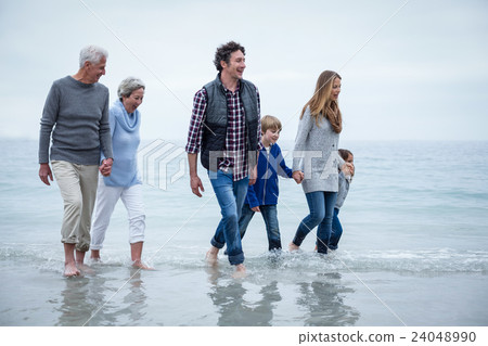 Multi-generation family walking in shallow water at beach 24048990