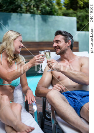 Couple sitting on sun lounger and toasting champagne glass Couple sitting on sun lounger and toasting champagne glass 24049108
