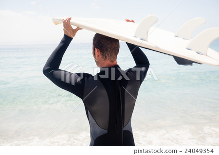 Rear view of surfer holding surfboard over head Rear view of surfer holding surfboard over head 24049354