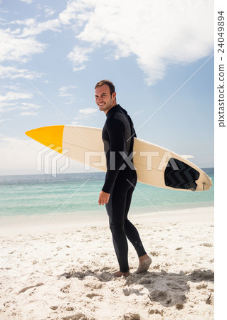 Happy surfer holding a surfboard on the beach Happy surfer holding a surfboard on the beach 24049894