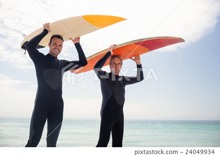 Portrait of happy father and son carrying a surfboard over their head Portrait of happy father and son carrying a surfboard over their head 24049934