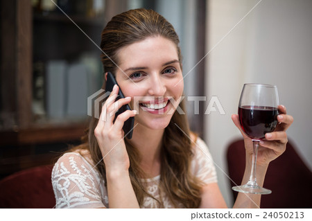 Portrait of woman holding wine glass while talking on phone Portrait of woman holding wine glass while talking on phone 24050213