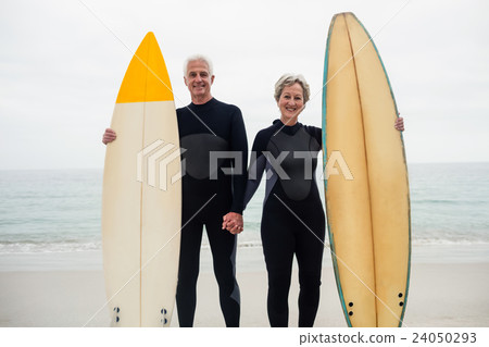 Portrait of senior couple with surfboard holding hand on the beach 24050293