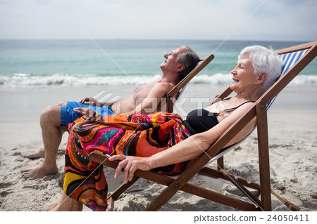 Happy senior couple relaxing on deckchairs at beach Happy senior couple relaxing on deckchairs at beach 24050411