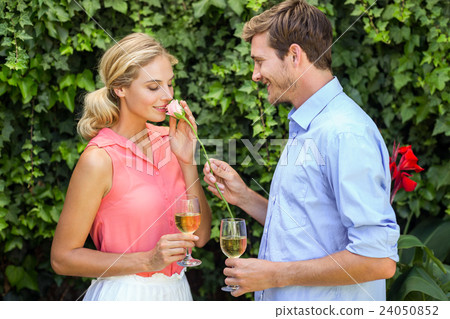 Young man giving flower to woman while holding wineglasses 24050852