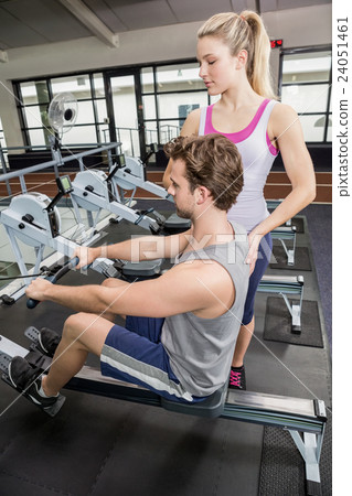 Female trainer assisting a man on rowing machine Female trainer assisting a man on rowing machine 24051461