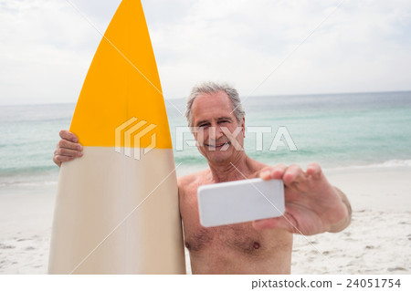 Senior man with surfboard taking a selfie on mobile phone Senior man with surfboard taking a selfie on mobile phone 24051754